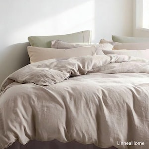 May include: A bed with a neutral-toned duvet cover and several pillows in shades of beige and green. The bedding has a soft, wrinkled texture, suggesting a linen or similar fabric. The scene is bathed in natural light, creating a serene and inviting atmosphere.
