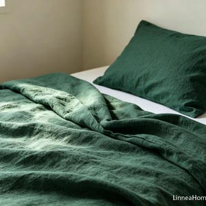 May include: A dark forest green bedding set consisting of a textured duvet cover and a matching pillowcase. The fabric has a visible weave and a soft, rumpled appearance. The brand name LinneaHome is printed in the bottom right corner.