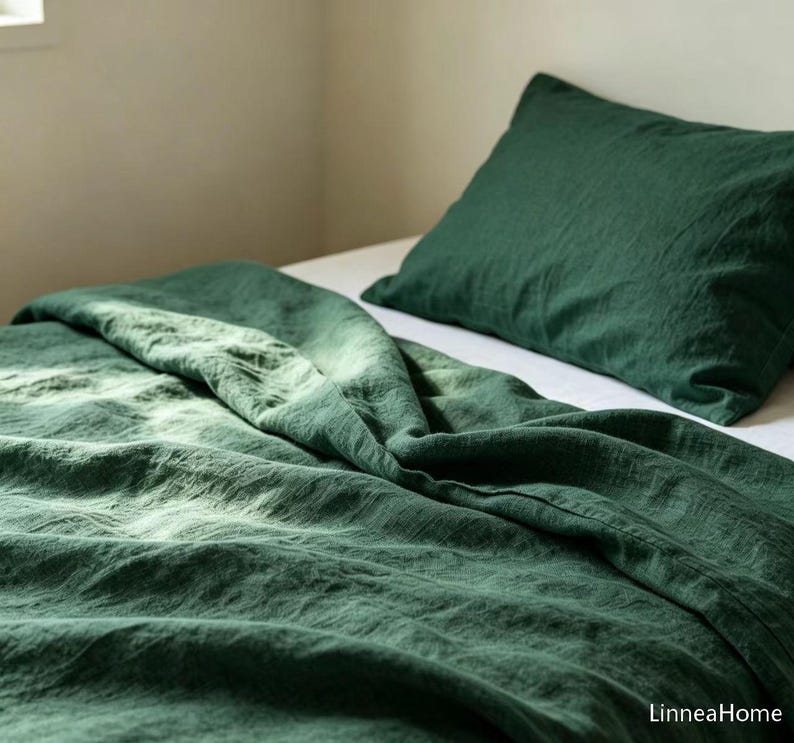 May include: A dark forest green bedding set consisting of a textured duvet cover and a matching pillowcase. The fabric has a visible weave and a soft, rumpled appearance. The brand name LinneaHome is printed in the bottom right corner.