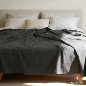 May include: A dark charcoal gray bedspread covers a bed with a light-colored headboard. The bed features two white pillows, two striped pillows, and one solid cream-colored pillow. The text LinneaHome is visible in the bottom right corner.