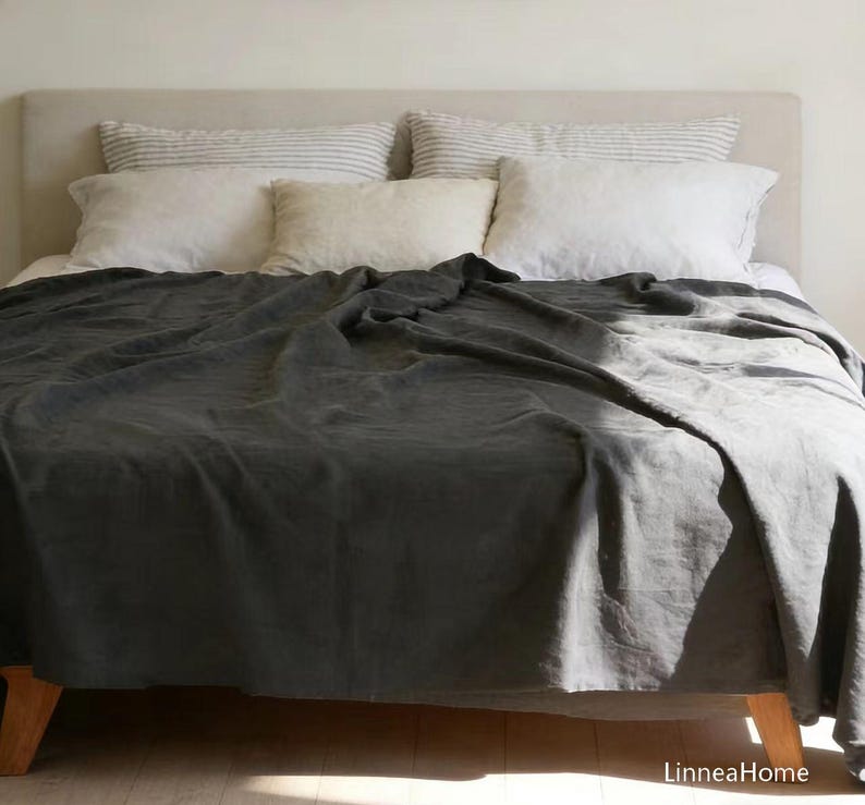 May include: A dark charcoal gray bedspread covers a bed with a light-colored headboard. The bed features two white pillows, two striped pillows, and one solid cream-colored pillow. The text LinneaHome is visible in the bottom right corner.