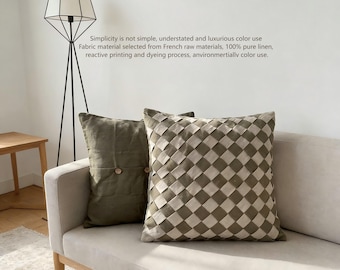 May include: Two decorative throw pillows on a beige sofa. One pillow is olive green with two wooden buttons. The other pillow has a woven, checkered design in shades of beige and olive green. Text on the wall reads: Simplicity is not simple, understated and luxurious color use.