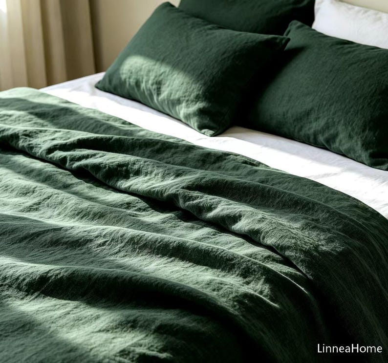 May include: A dark forest green bedding set featuring a duvet cover and two matching pillowcases. The fabric has a visible textured weave and is layered over white sheets. The text LinneaHome is printed in the bottom right corner of the image.