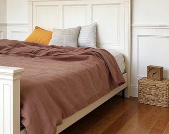 May include: A white bed frame with a matching headboard is covered with a brown comforter. Pillows in yellow, gray, and white stripes rest against the headboard. A woven basket and a wooden clock sit on the floor.