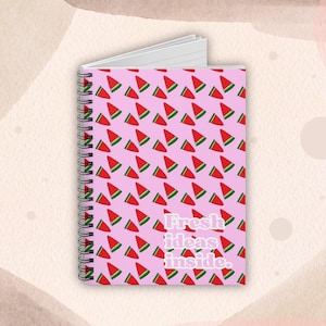 Puede incluir: Cuaderno de espiral con una cubierta rosa con un patrón de rodajas de sandía rojas y verdes. El texto "Fresh ideas inside" está impreso en blanco. Tiene una encuadernación en espiral plateada y páginas de papel blanco.