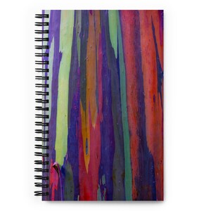 May include: A spiral-bound notebook featuring a vibrant, multi-colored vertical striped pattern on the cover. The design displays a spectrum of colors including deep purple, bright orange, lime green, and red, mimicking the texture of tree bark.