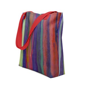 May include: A tote bag featuring a vertical striped pattern in shades of purple, orange, red, and light green. The bag has two bright red fabric handles attached to the top, providing a contrast to the multicolored body of the bag.