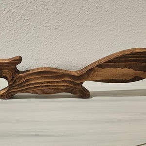 May include: A wooden figurine shaped like a squirrel in a running pose, featuring a natural brown wood grain pattern with darker brown streaks throughout the body and a large, elongated tail extending horizontally from the back of the figure.
