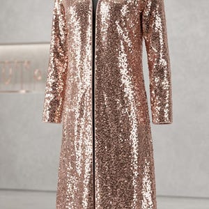 May include: A long, rose gold sequin duster coat with long sleeves and a V-neck. The coat is displayed on a mannequin against a neutral background. The sequins create a shimmering effect.