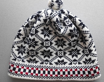 May include: A knitted winter hat with a white base and a repeating pattern of navy blue star-like shapes. The brim features a red, white, and navy blue checkered design. A matching pom-pom sits atop the hat.