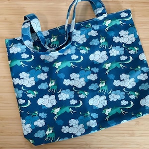 Puede incluir: Una bolsa de tela azul con un patrón blanco y azul de nubes y animales estilizados. La bolsa tiene dos asas.