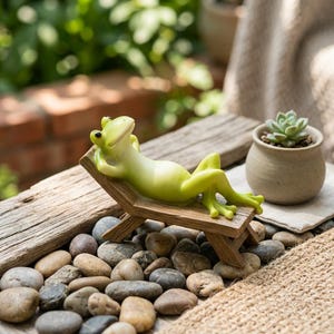 May include: A light green frog figurine relaxing on a miniature wooden lounge chair. The frog is positioned on a wooden surface, surrounded by small stones and a small potted succulent. The figurine has its arms behind its head, appearing relaxed.