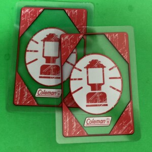 May include: Two Coleman-branded playing cards featuring a red and white lantern design on a green background. The cards have a distressed, vintage look with red accents and the Coleman logo.