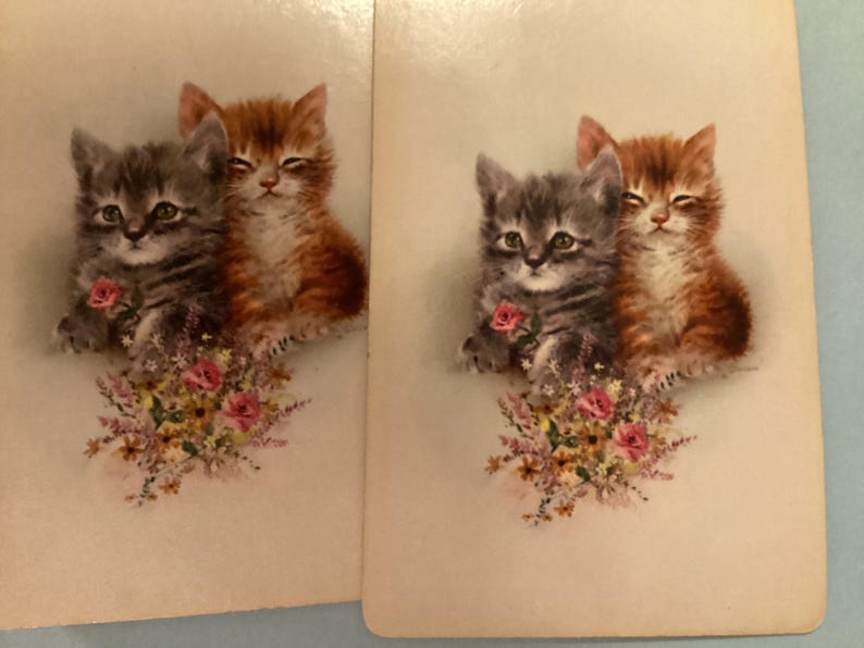 May include: Two vintage-style cards featuring illustrations of kittens. One kitten is gray and the other is orange, both with closed eyes. They are positioned above a bouquet of pink roses and other flowers.