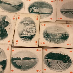 May include: A selection of antique playing cards with sepia-toned landscape illustrations. The cards depict scenes such as waterfalls and bridges. The suits and numbers are visible on the cards.