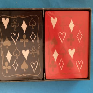 May include: A deck of playing cards in a black box. The cards are divided into two stacks, one black and one red. Each card features white suit symbols: hearts, diamonds, clubs, and spades.