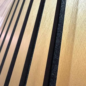 May include: Close-up of a gold-colored panel with vertical black stripes. The panel has a textured surface and a repeating pattern of gold and black. The gold sections have a subtle, brushed appearance.