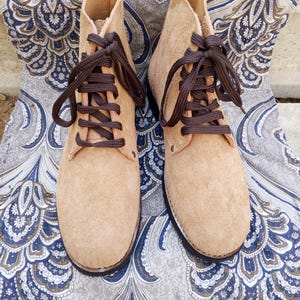 May include: A pair of tan suede ankle boots with brown laces. The boots have a classic design with a rounded toe and a sturdy sole. The laces are tightly tied, and the boots appear to be unworn.