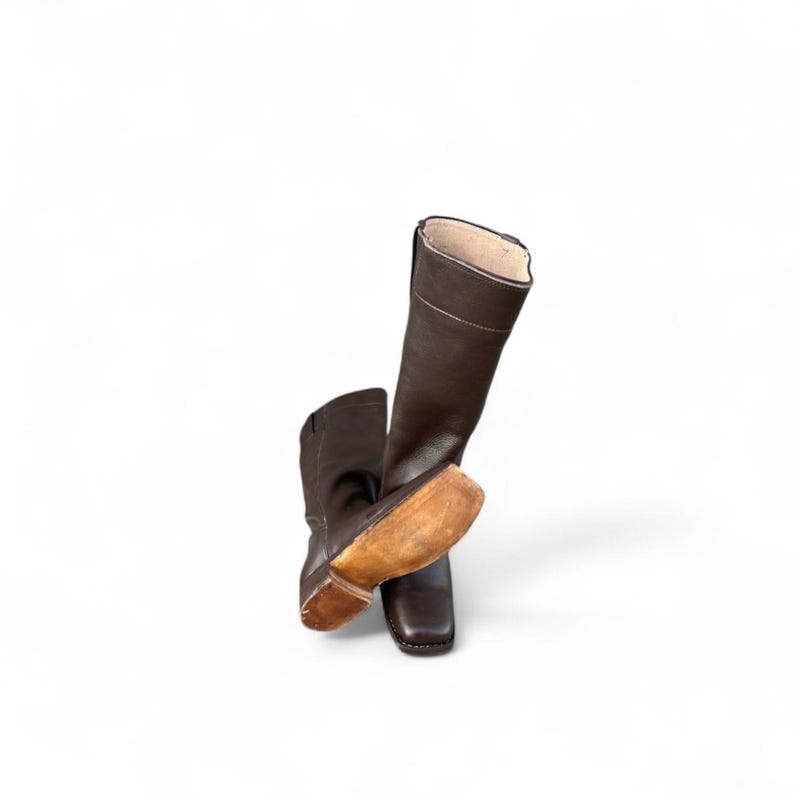 May include: A pair of brown leather riding boots. The boots have a tall shaft, a square toe, and a light-colored sole. The boots are angled against a white background.
