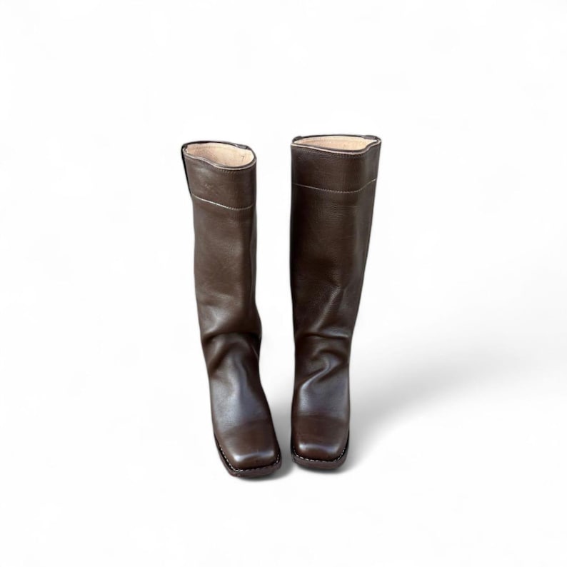 May include: A pair of brown leather riding boots. The boots are knee-high with a square toe and a slight heel. The leather has a smooth texture and a rich, dark brown color. The interior lining is a lighter tan color.