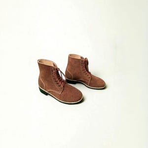May include: A pair of brown suede ankle boots with laces. The boots have a rounded toe, a black sole, and a white trim. The boots are set against a white background.