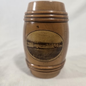 May include: A small, brown, barrel-shaped container with horizontal grooves. An oval image of a pier and boats is on the front, with the text "WALMARIA PIER" below. The container is made of wood.