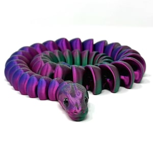 May include: A 3D-printed articulated snake toy in shades of purple, green, and blue. The snake is coiled, with a detailed head and segmented body. The toy is designed to be flexible and poseable.