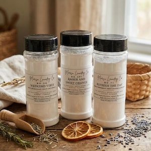 Może przedstawiać: Trzy przezroczyste plastikowe słoiki z czarnymi pokrywkami, z etykietami "Weekend Vibes", "Amber and Sweet Orange" i "Refresh the Day". Słoiki stoją na drewnianej powierzchni z suszonymi plasterkami pomarańczy, rozmarynem i drewnianą łyżką.