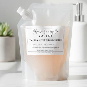 May include: A clear pouch of Marsu Laundry Co. Vanilla Sweet Orange Refill. The pouch contains a light orange liquid and has a white label with black text. The label reads "FOAMING HAND SOAP REFILL" and "HAND POURED TO 37 OZ."