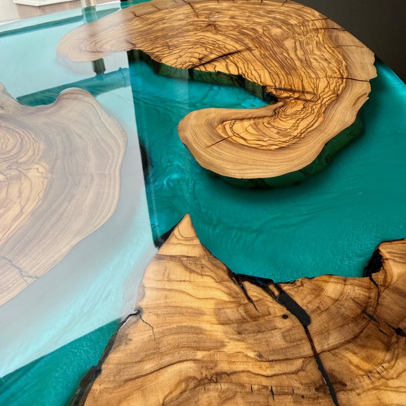 May include: A handcrafted wooden table with a teal epoxy resin river. The table features natural wood grain patterns and a glossy finish. The wood sections are irregularly shaped, creating a unique design.