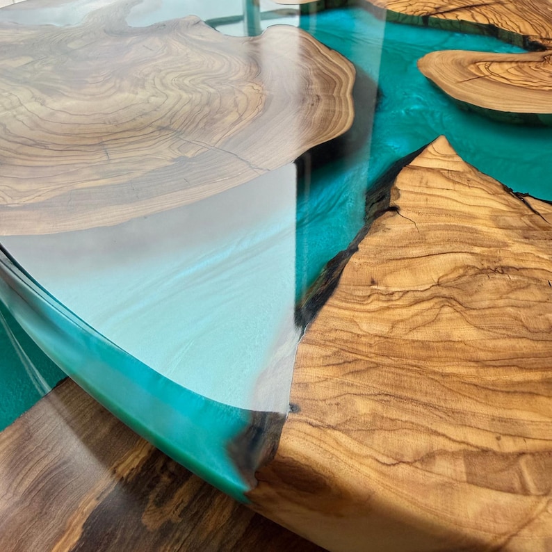 May include: A handcrafted wooden table with a unique design. The table features sections of natural wood with a light brown color, interspersed with a vibrant turquoise resin. The resin creates a river-like effect, adding a modern touch to the rustic aesthetic.