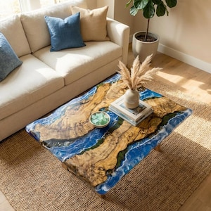 Pode incluir: Uma mesa de centro retangular com um design único. O tampo apresenta uma combinação de madeira e resina azul, assemelhando-se a uma cena costeira. A mesa tem aproximadamente 100 cm de comprimento e 50 cm de largura, com um padrão de grão de madeira natural. A mesa está sobre um tapete tecido.