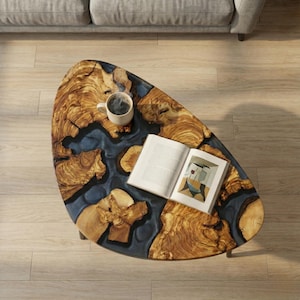 May include: Oval coffee table with a unique design. The table features a wooden surface with a blue resin river, a cup of coffee, and an open book. The table is approximately 48 inches long.