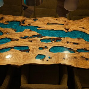 May include: A handcrafted wooden table with a live edge design. The table features a natural wood grain with turquoise resin inlays, creating a river-like effect. The table is a unique piece of furniture.