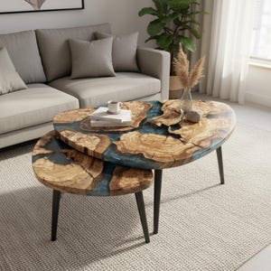 Könnte beinhalten: Zwei ovale Couchtische mit einem einzigartigen Design. Die Tischplatten weisen ein natürliches Holzmaserungsmuster mit einem blauen Harzfluss auf. Die Tische haben schwarze Metallbeine und sind in einer verschachtelten Konfiguration angeordnet.