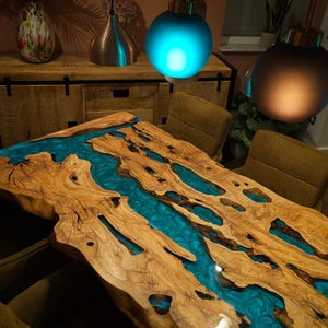 May include: A handcrafted wooden table with a river of turquoise resin flowing through the center. The live edge table is made of light brown wood with natural knots and imperfections. The table is a unique piece of furniture.