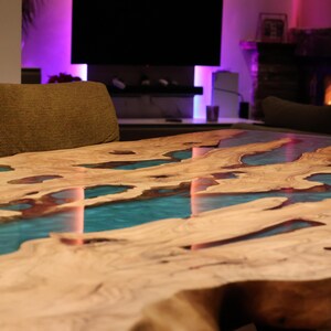 May include: A handcrafted wooden coffee table with a unique design. The table features a natural wood grain surface with turquoise resin inlays, creating a river-like effect. The table is a statement piece for any living room.