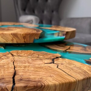 May include: Two wooden tables with a turquoise resin inlay. The tables have a natural wood grain and a smooth, glossy finish. The resin creates a striking contrast with the wood, adding a modern touch to the design. The tables are round and appear to be stacked.