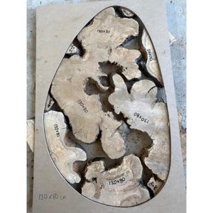 May include: A wooden table top with a unique, organic shape. The surface is made of light brown wood with a dark, resin-filled center. The dimensions are 130 x 80 cm, as indicated on the surface. The design features irregular, flowing shapes.