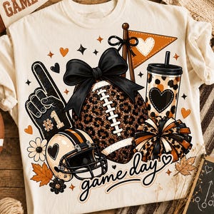 Könnte beinhalten: Ein cremefarbenes T-Shirt mit einem Grafikdruck eines Footballs im Leopardenmuster mit einer großen schwarzen Schleife, einem Schaumstofffinger mit der Nummer eins, einem Helm, einem Becher im Leopardenmuster, einem Pompon und einem Wimpel mit dem Text game day.