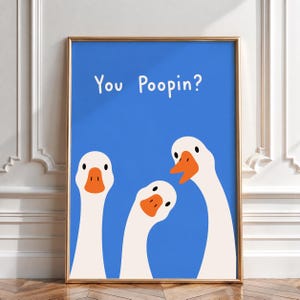 May include: A framed wall art print featuring a bright blue background with three white geese with orange beaks. The text "You Poopin?" is printed in white, sans-serif letters at the top centre of the blue field above the three geese illustrations.