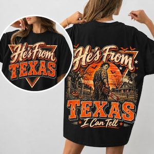 May include: A black t-shirt featuring a graphic print of a horror movie character holding a chainsaw in front of a house at sunset. The text reads He's from TEXAS I Can Tell in orange and white lettering, with bats and pumpkins in the background.