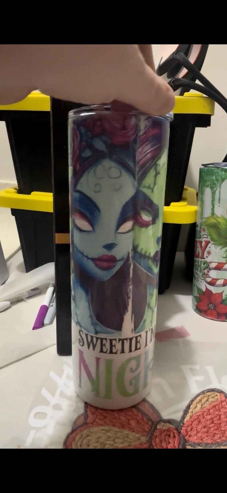 Puede incluir: Un vaso cil&iacute;ndrico con una ilustraci&oacute;n espeluznante de un personaje con piel azul, labios rojos y boca cosida. El vaso tiene el texto "Sweetie Night" impreso. El dise&ntilde;o es una mezcla de azul, verde y morado.