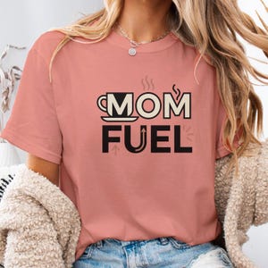 Mom Fuel retro coffee typography graphic t-shirt printed on Comfort Colors garment-dyed vintage washed heavyweight tee featuring coffee cup M letterform with steam lines and energy arrows in terracotta black and cream
