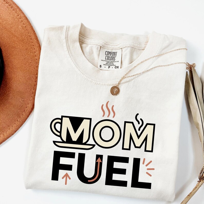 Mom Fuel retro coffee typography graphic t-shirt printed on Comfort Colors garment-dyed vintage washed heavyweight tee featuring coffee cup M letterform with steam lines and energy arrows in terracotta black and cream