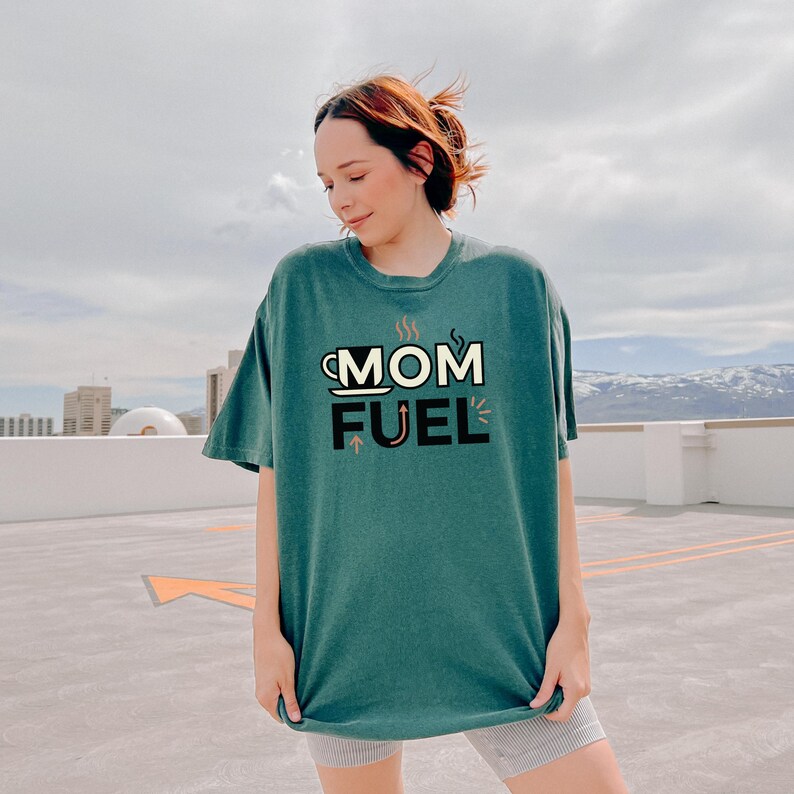 Mom Fuel retro coffee typography graphic t-shirt printed on Comfort Colors garment-dyed vintage washed heavyweight tee featuring coffee cup M letterform with steam lines and energy arrows in terracotta black and cream