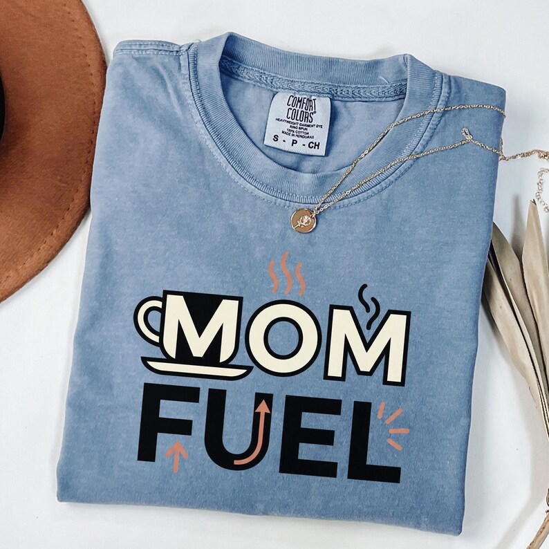 Mom Fuel retro coffee typography graphic t-shirt printed on Comfort Colors garment-dyed vintage washed heavyweight tee featuring coffee cup M letterform with steam lines and energy arrows in terracotta black and cream