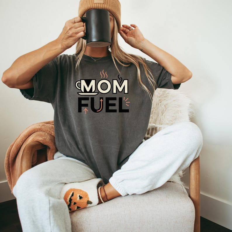 Mom Fuel retro coffee typography graphic t-shirt printed on Comfort Colors garment-dyed vintage washed heavyweight tee featuring coffee cup M letterform with steam lines and energy arrows in terracotta black and cream