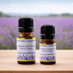 May include: Two amber glass bottles of lavender essential oil with black caps. The labels read "Lavender Essential Oil" and "Leaning Tree Lavender Farm." The background shows a lavender field.