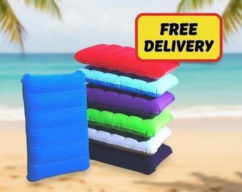 May include: A stack of colorful inflatable pillows in red, light blue, purple, green, white, and navy blue. A single blue pillow stands upright on the left. The background shows a beach scene with palm trees and the ocean. A yellow sign with the words "FREE DELIVERY" is in the top right.